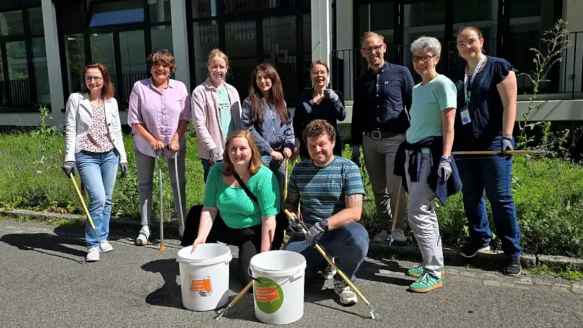 Mitarbeiter:innen sammeln Zigarettenkippen vor dem Dienstgebäude