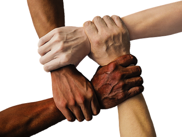 Symbolbild Diversity: Hände verschiedener Hautfarben fassen sich an die Handgelenke und bilden ein Viereck